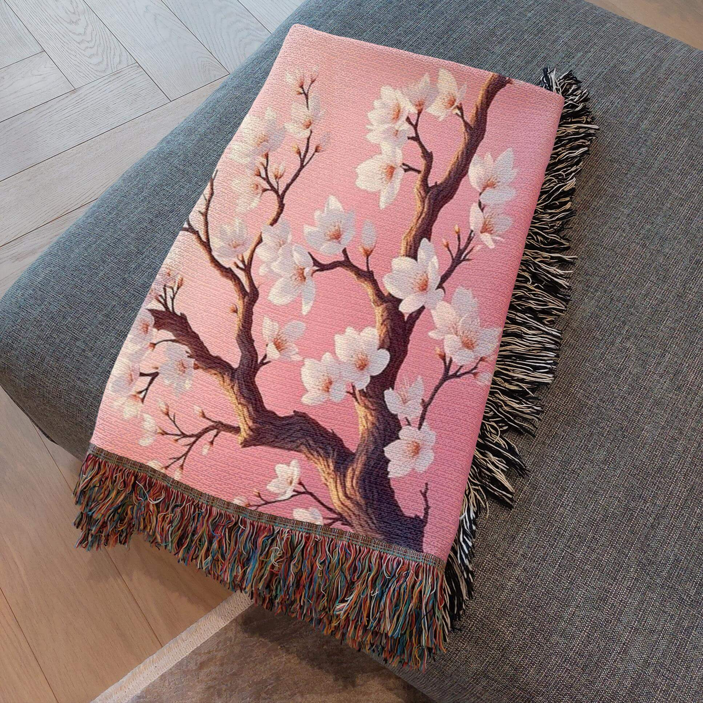 Pink Almond Blossom Woven Blanket folded and resting on a gray ottoman