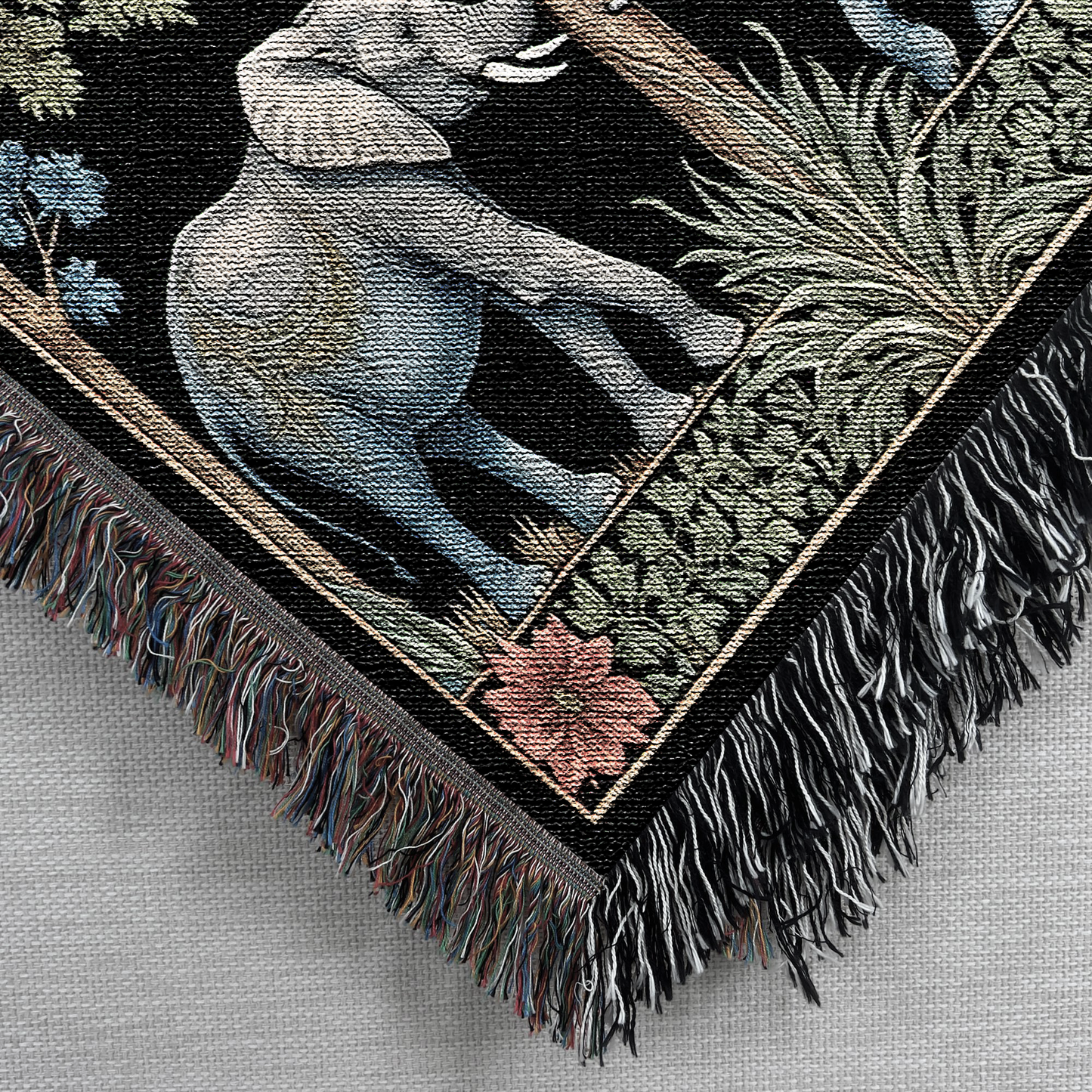 Closeup corner view of the Elephant Love Woven Blanket Tapestry featuring playful elephants and vibrant foliage detail.