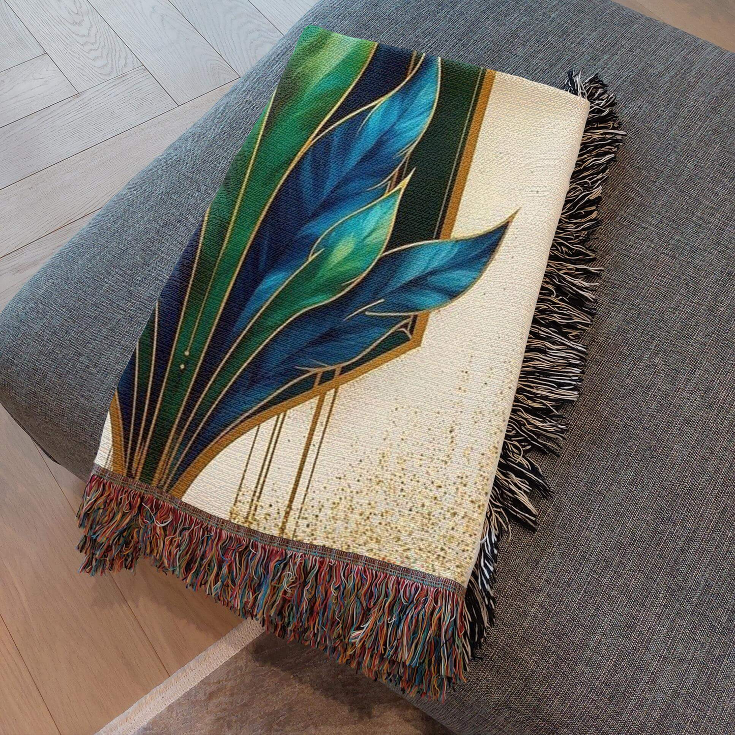 Art Deco Woven Blanket in Blue Green Gold draped on a couch, showcasing intricate leaf patterns and colorful fringes.