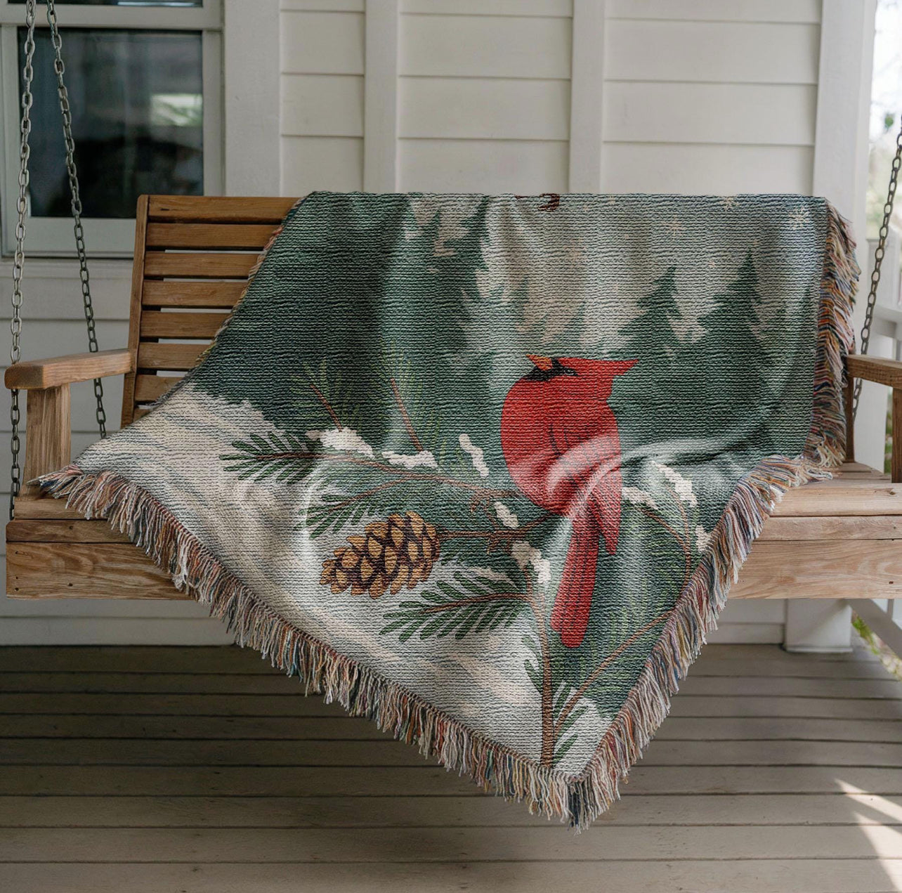 Matching blanket to the Cardinal Winter Scene woven pillow. The blanket is draped over a wood porch swing.