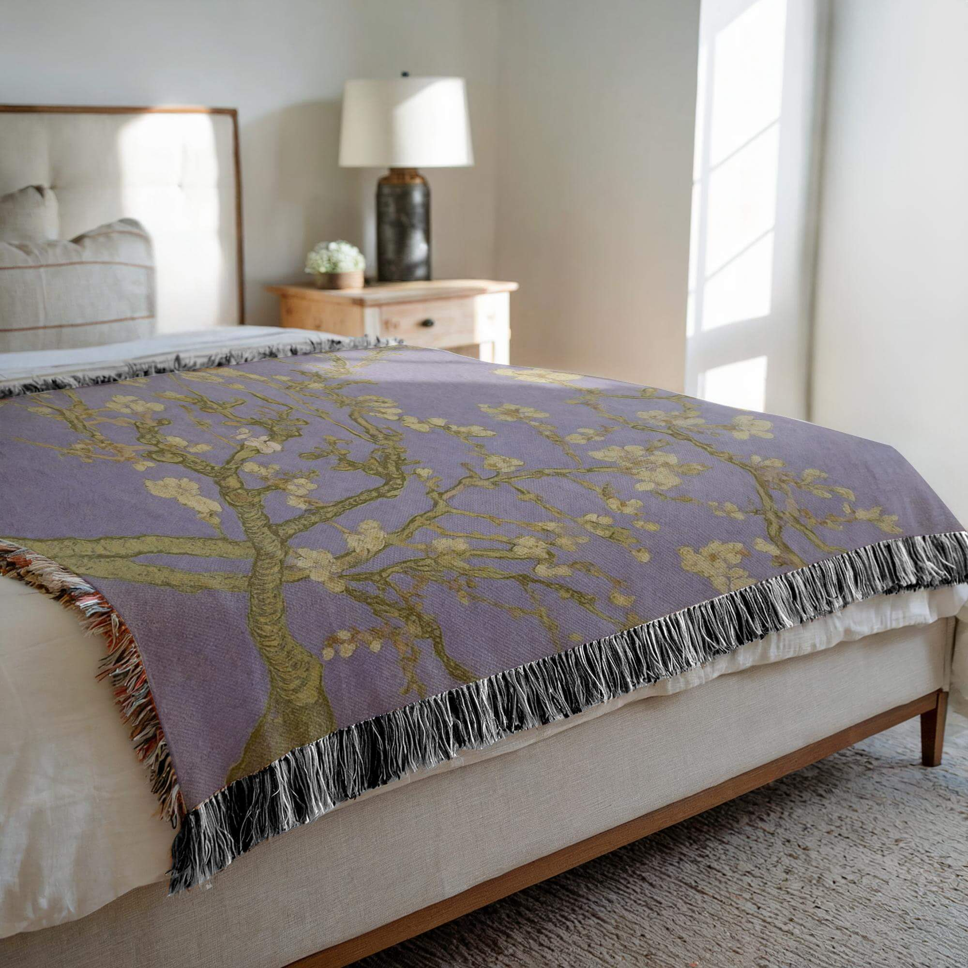 Lavender Almond Blossom Woven Blanket draped over a bed, featuring delicate ivory blossoms on a lavender background.