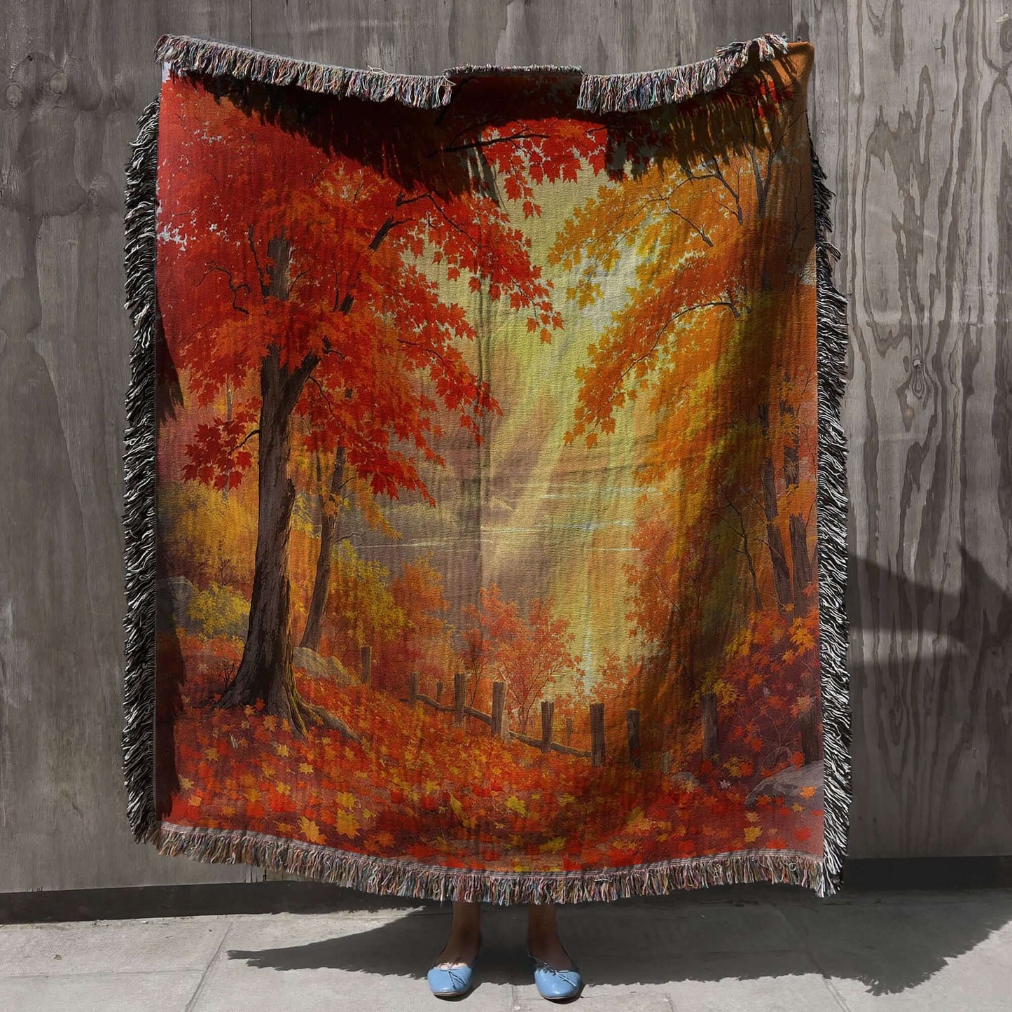 Person holding up the Autumn Day Woven Blanket Tapestry against a gray wall.