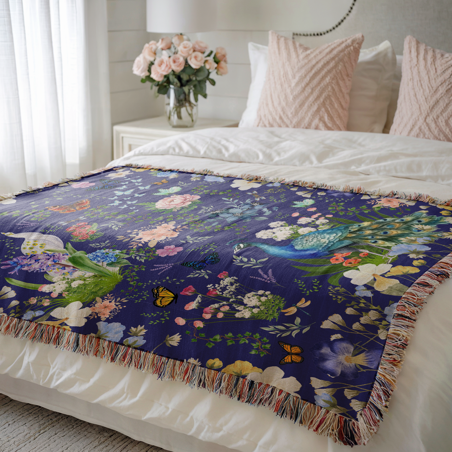 Blue Peacock Floral Woven Blanket with Fringes on a bed with pink pillows and a window near 