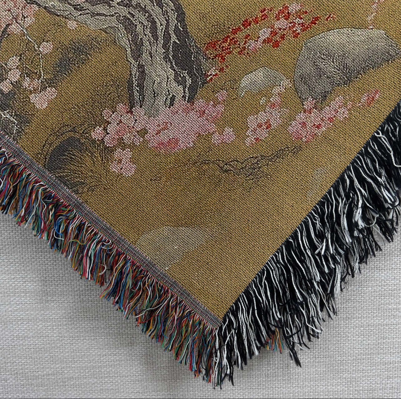 Closeup view of the corner of the Cherry Blossom Tree Woven Blanket Tapestry featuring an image of a cherry blossom tree.