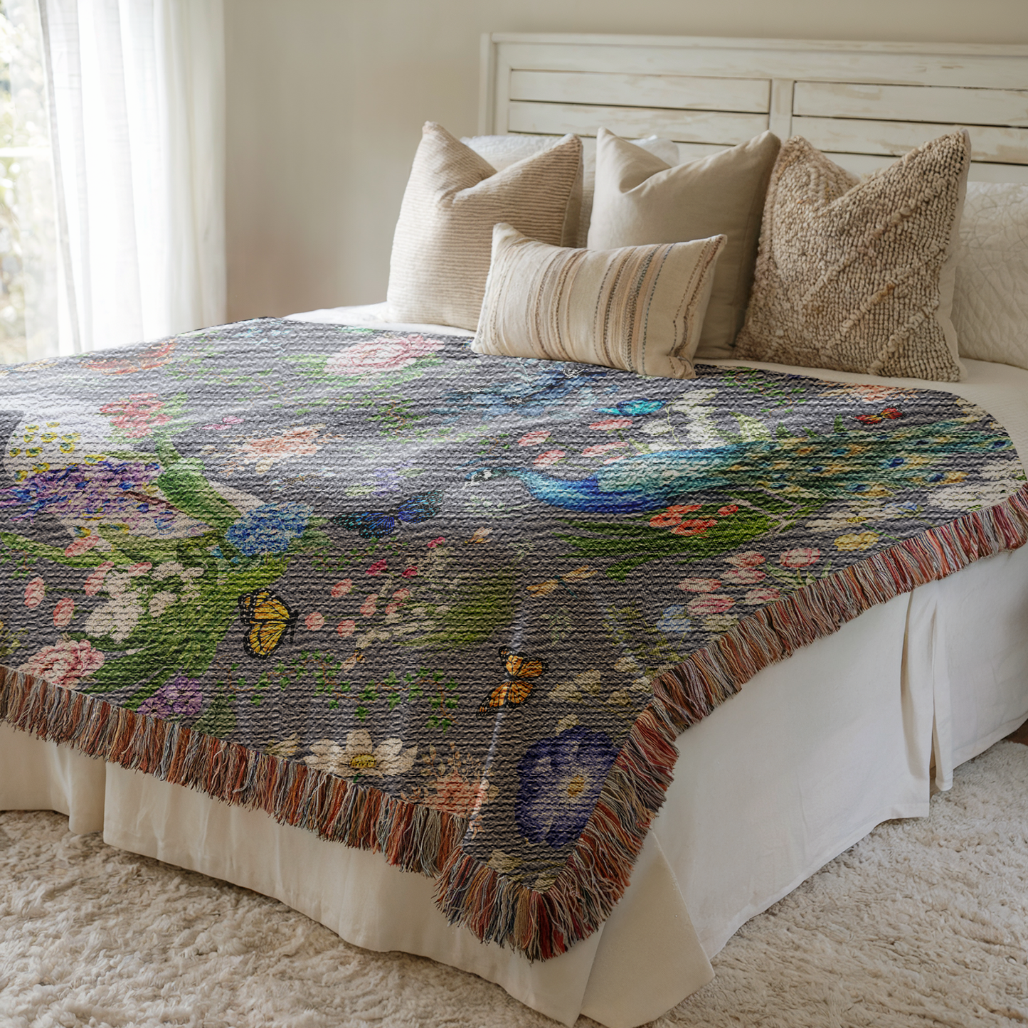 Dark Gray Peacock Floral Woven Blanket with Fringes draped over a bed with beige pillows in a bright bedroom