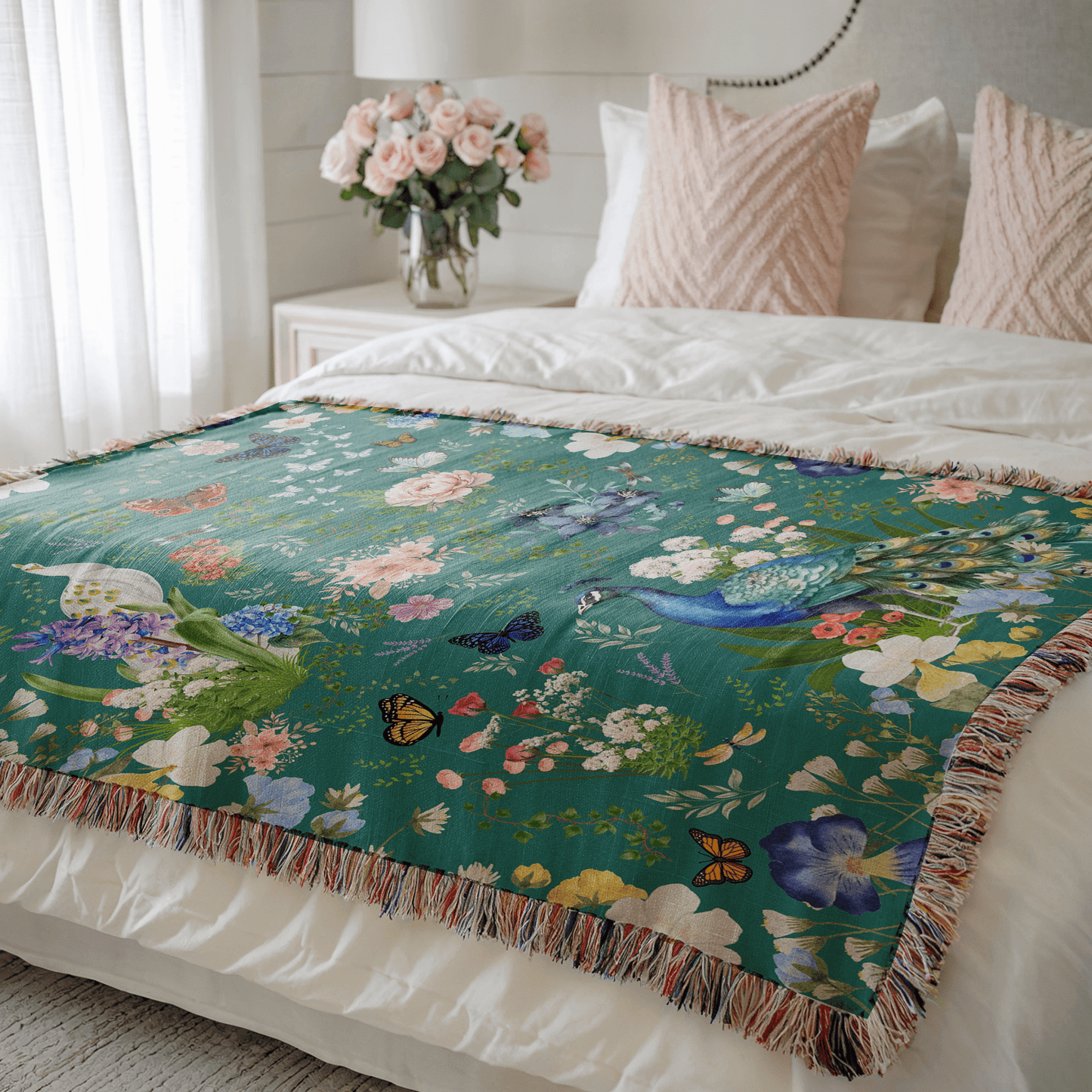 Teal Peacock Floral Woven Blanket with Fringes on a bed with pillows and flowers in the background.
